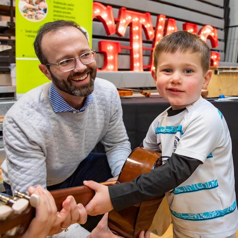  A young student holds a guitar with help from his father